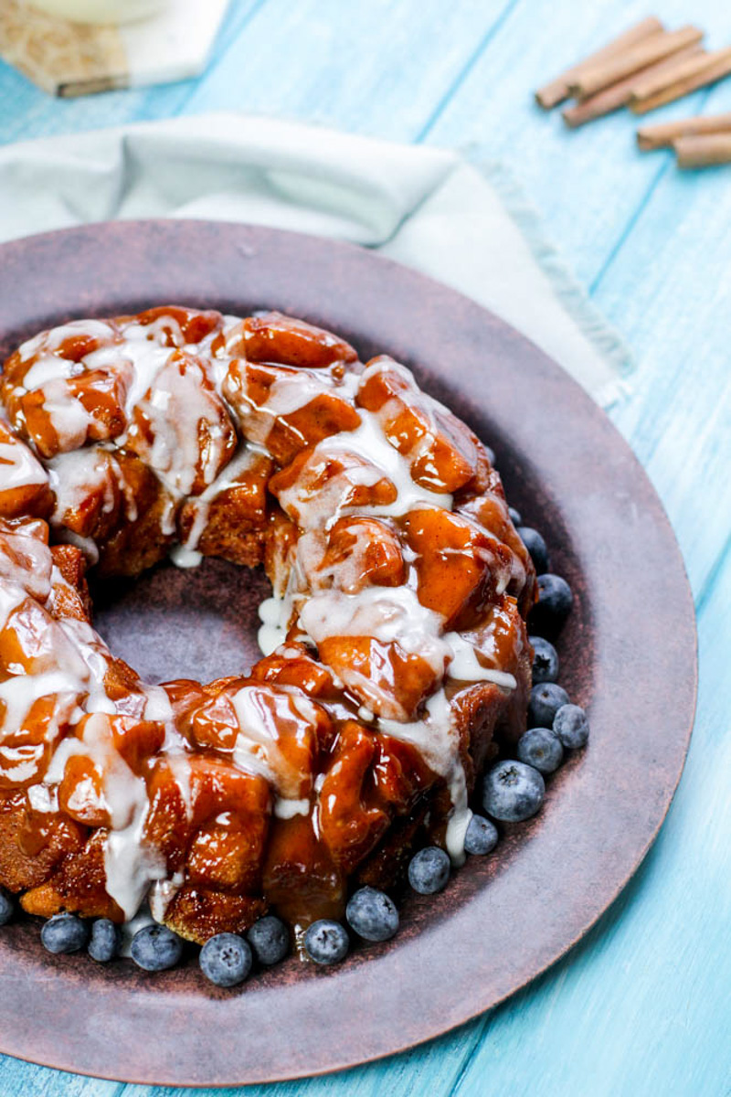 Ring of monkey bread on wooden plate surrounded by fresh blueberries. 