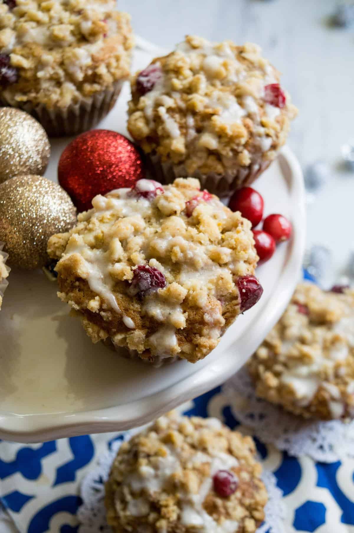 Muffins on a white cake plate with ornaments around  and fresh cranberries. 