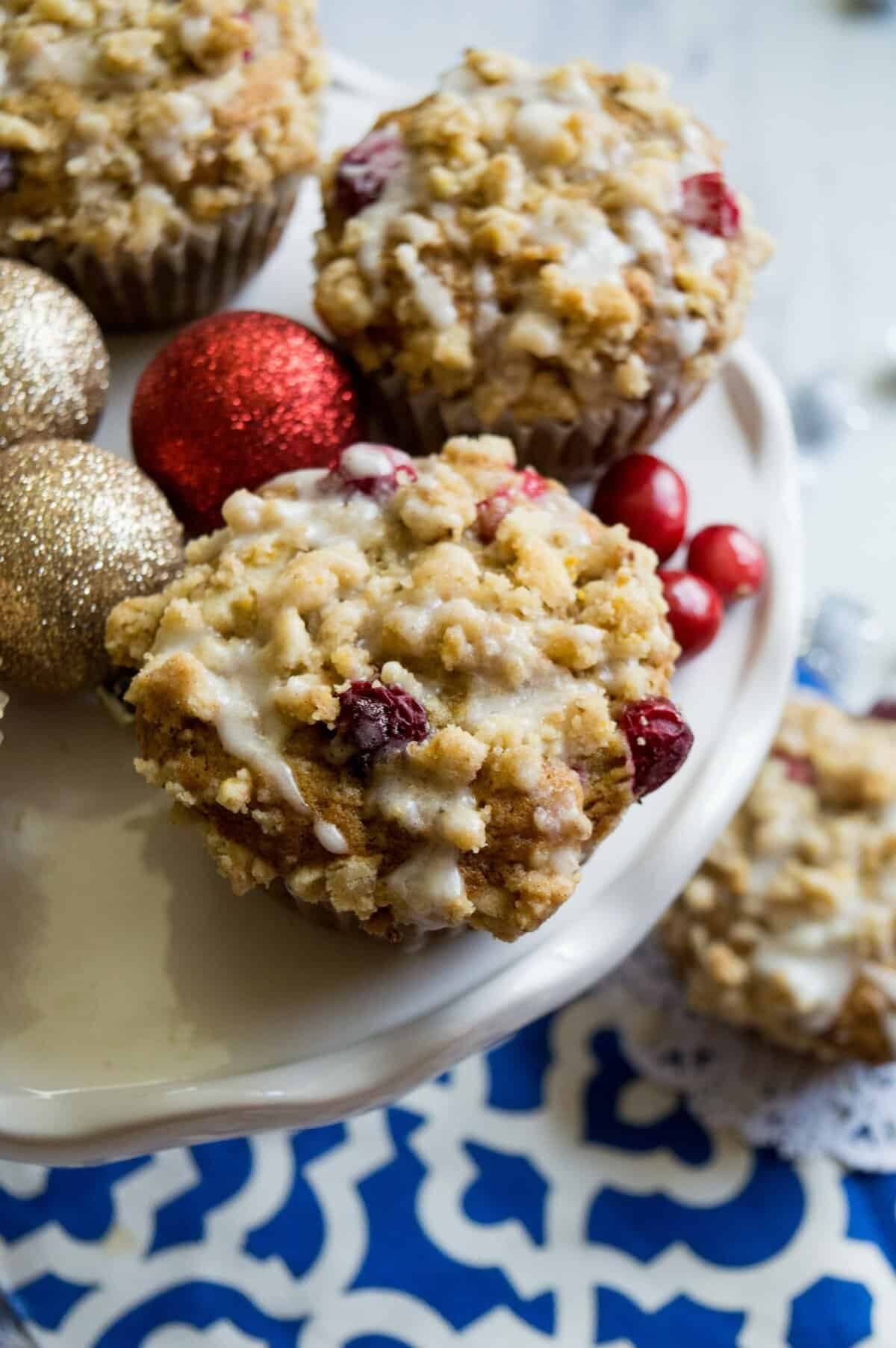 Cranberry orange muffins on white cake plate with blue dish towel underneath. 