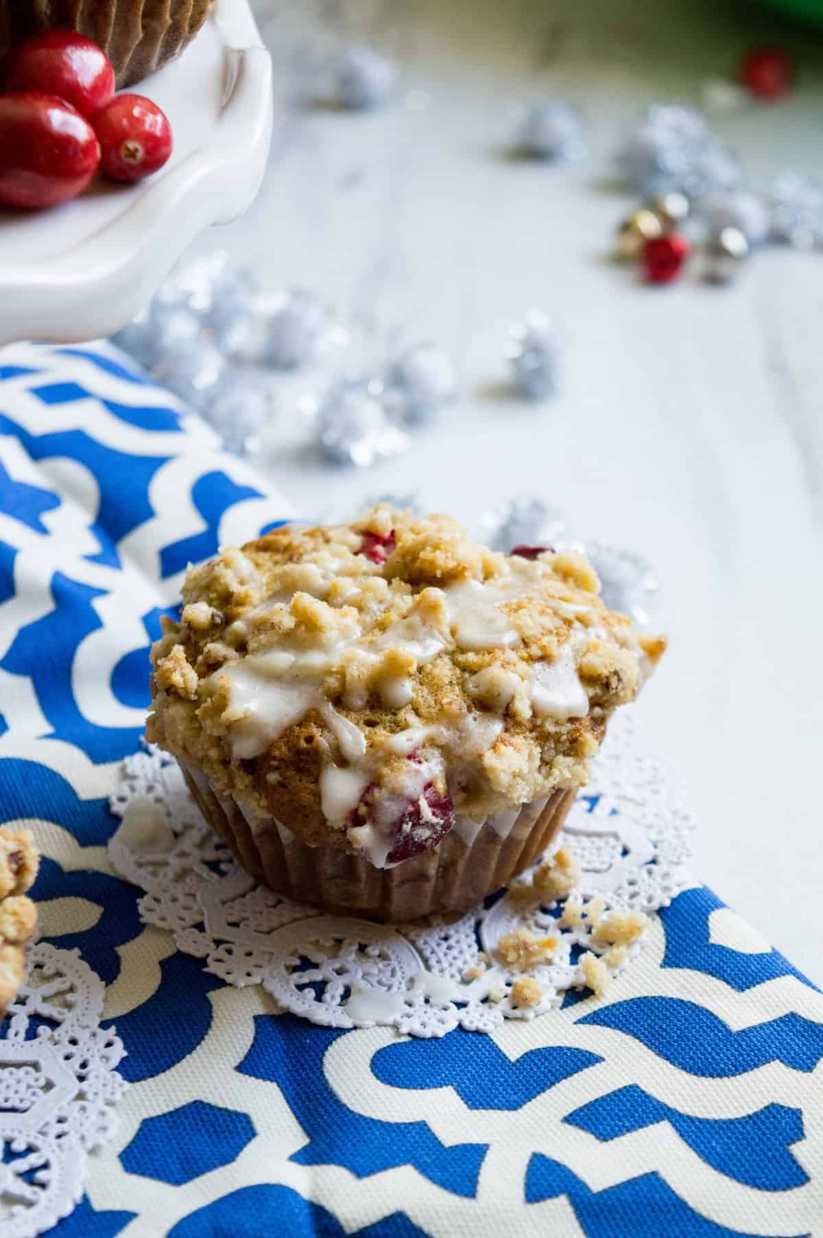 Single muffin on a blue and white dish towel with cranberries in background. 