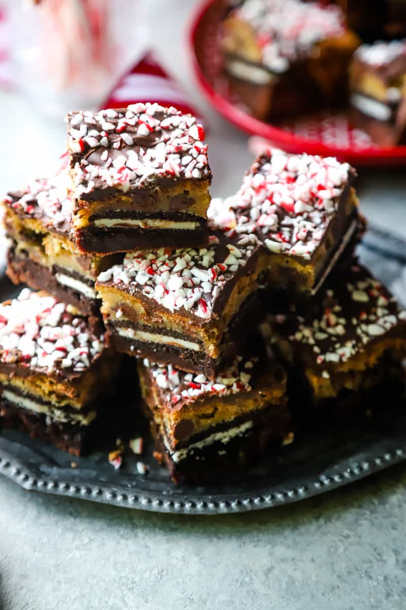 Four layer cookie brownie bars on a metal tray with red plate in the background. 