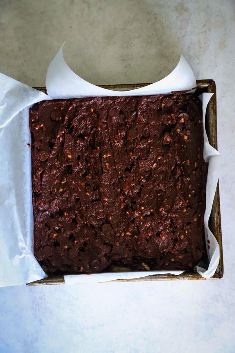 Brownie batter in a square parchment paper line pan. 