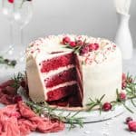 Square image of the cream cheese frosted cake with a slice out to expose red layers.