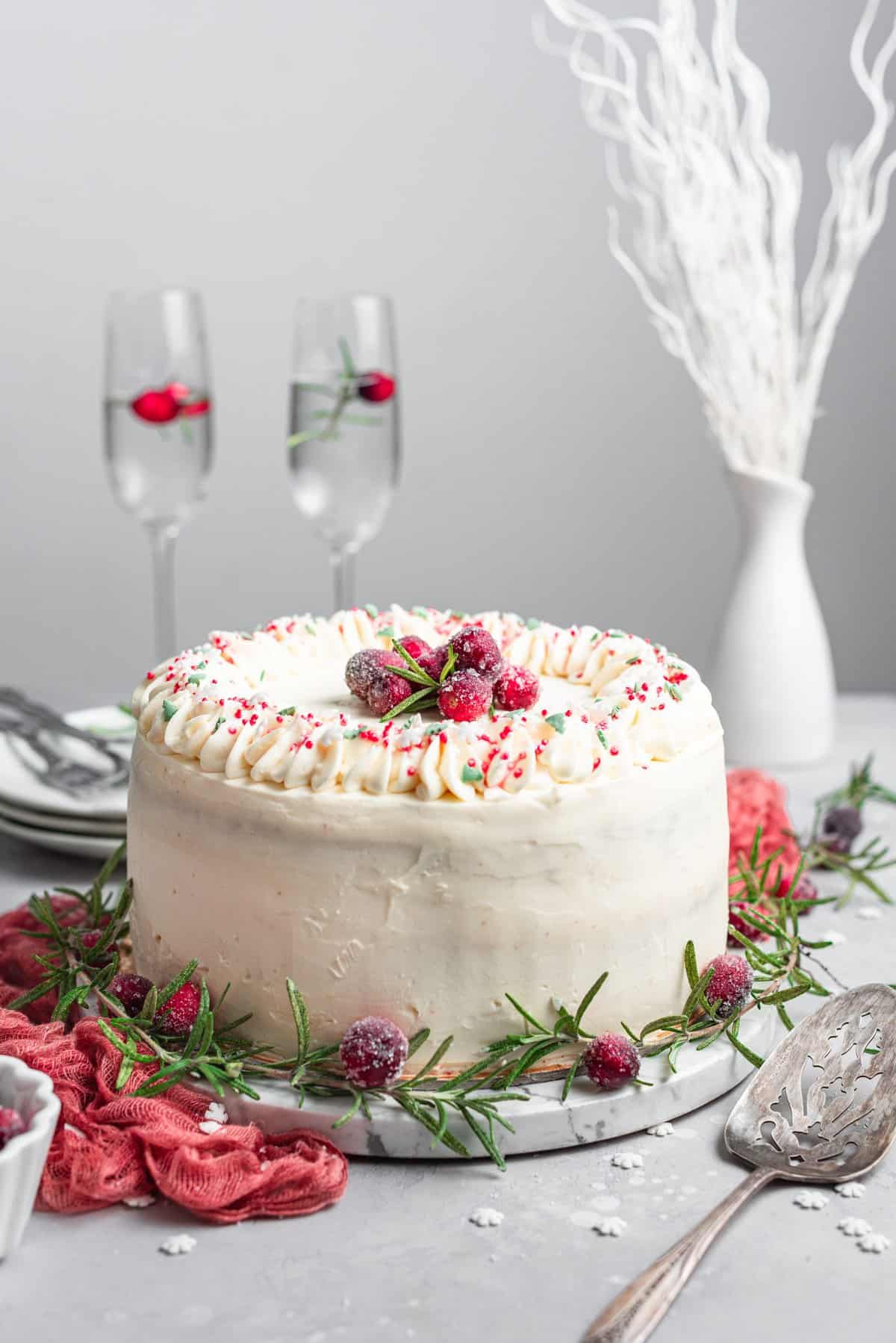 Full cake decorated with sugared cranberries and sprinkles on white marble cake plate. 