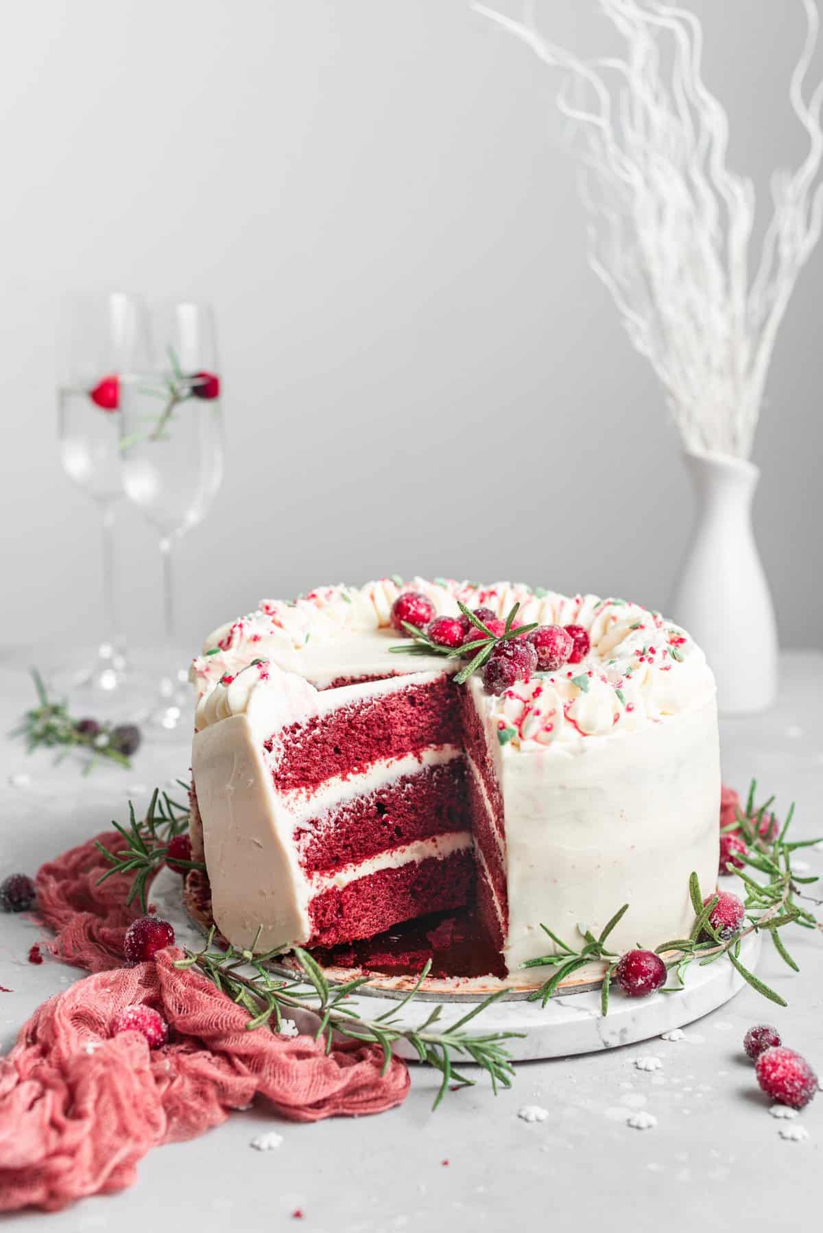 Cake partially cut into slices showing the red velvet layers on white cake plate. 