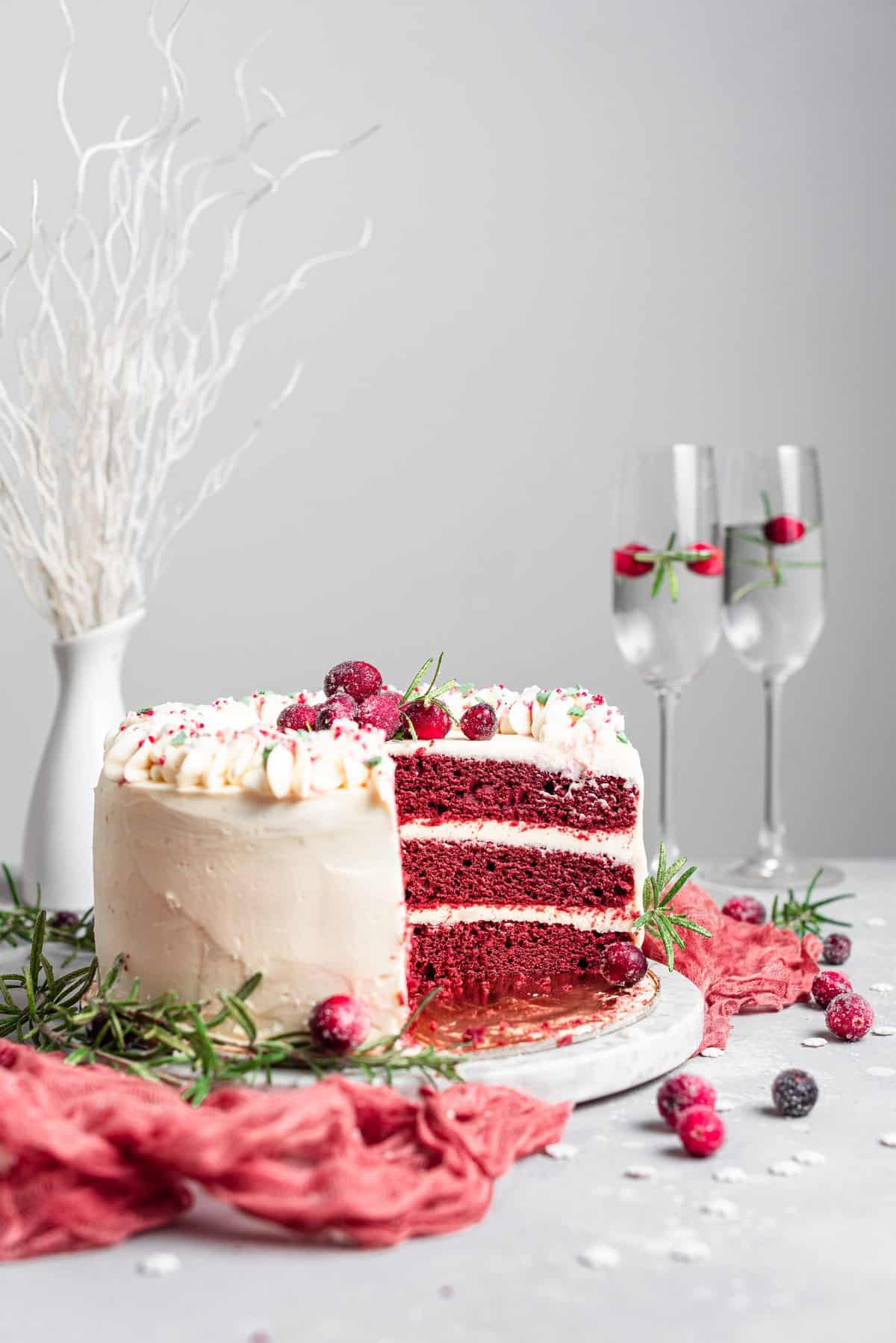Cake partially cut and exposing the red layers on white cake plate with champagne flutes in background. 