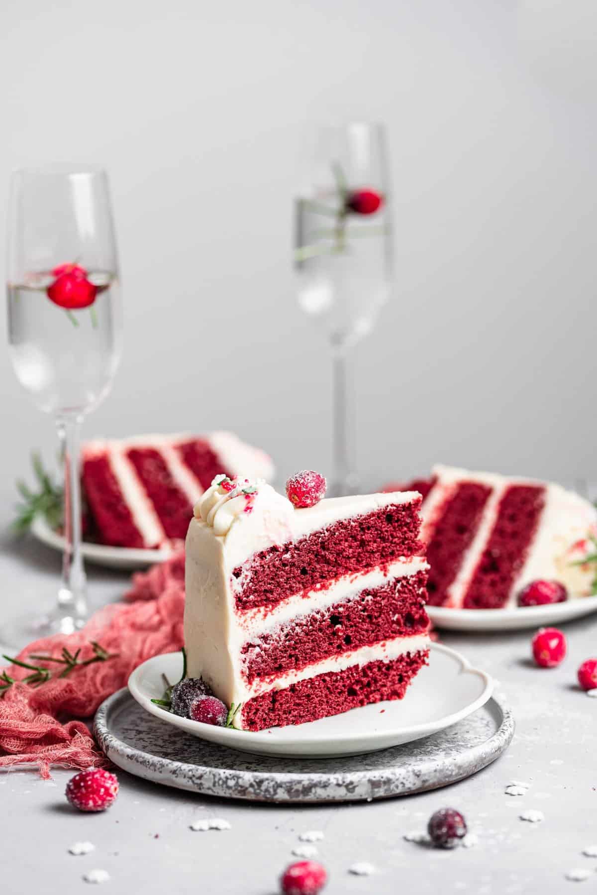 three slices of red velvet cake on white plates with champagne flutes in the background. 