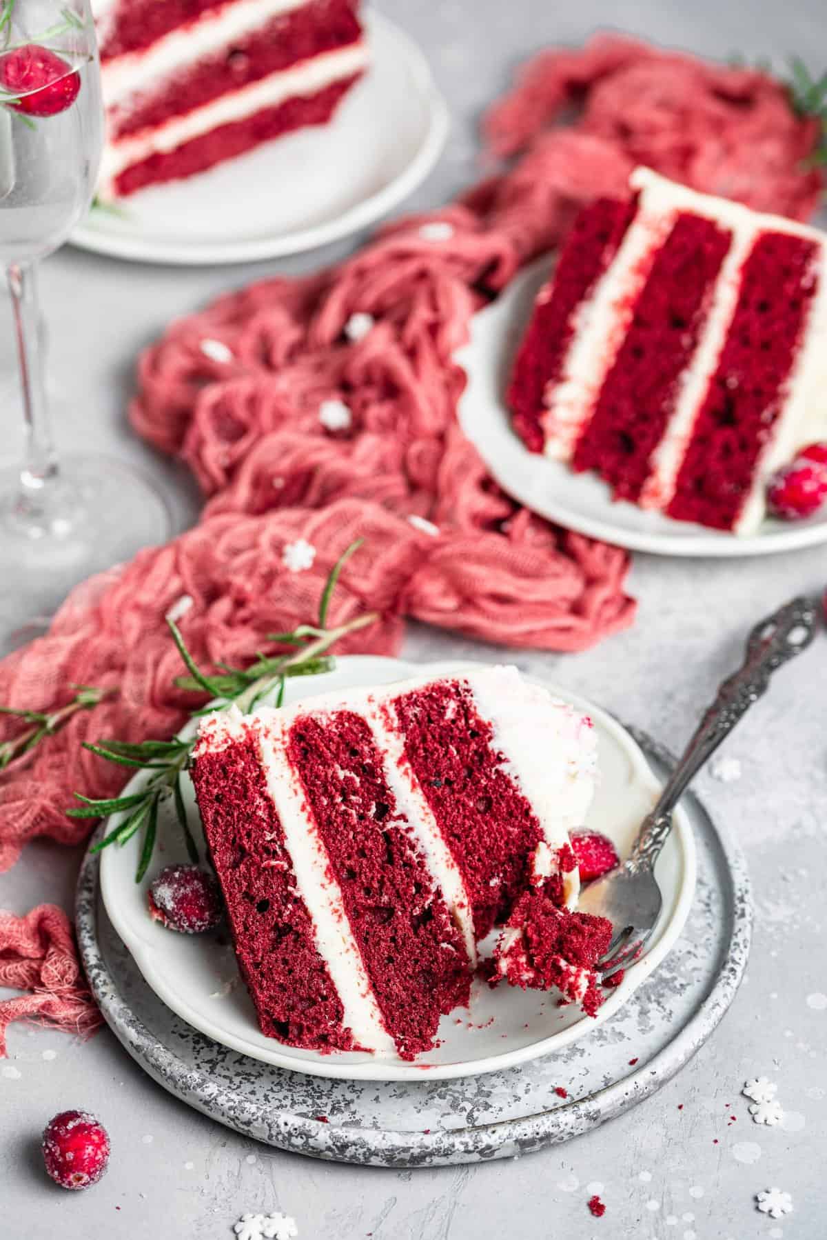 Three slices of red velvet cake on white plates with red dishtowel down the center. 