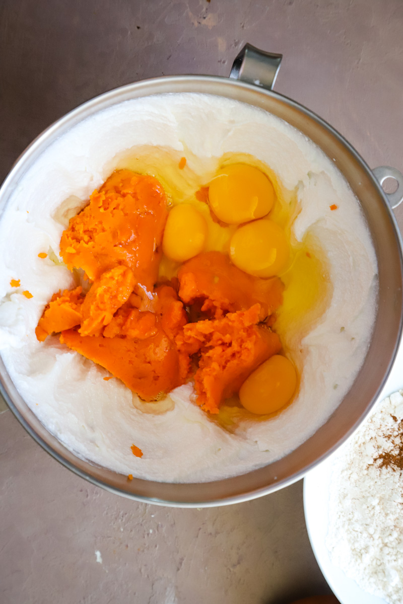Adding eggs and sweet potato puree to the creamed butter and sugar in metal bowl. 