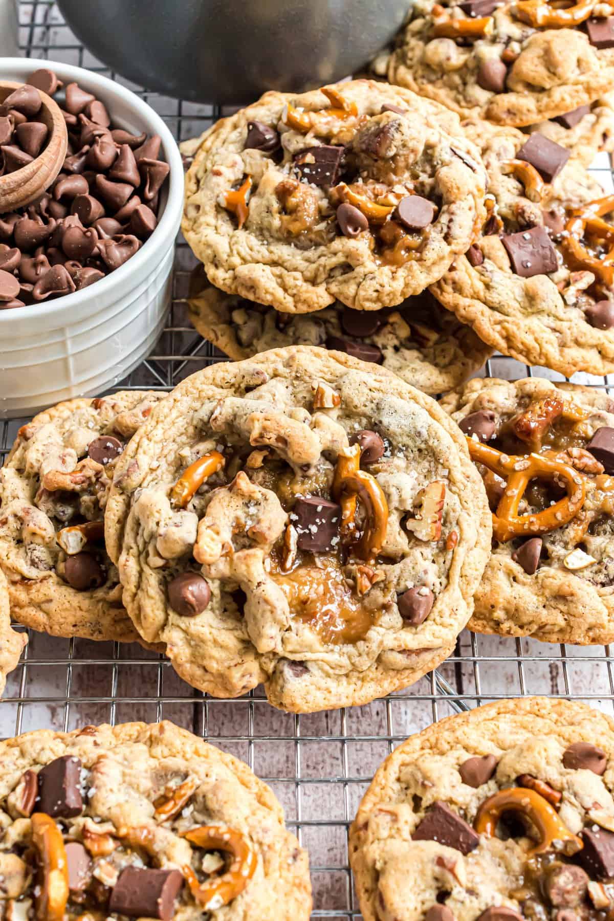 Cookies with pretzels and chocolate chips on a wire rack and bowl of chocolate. 