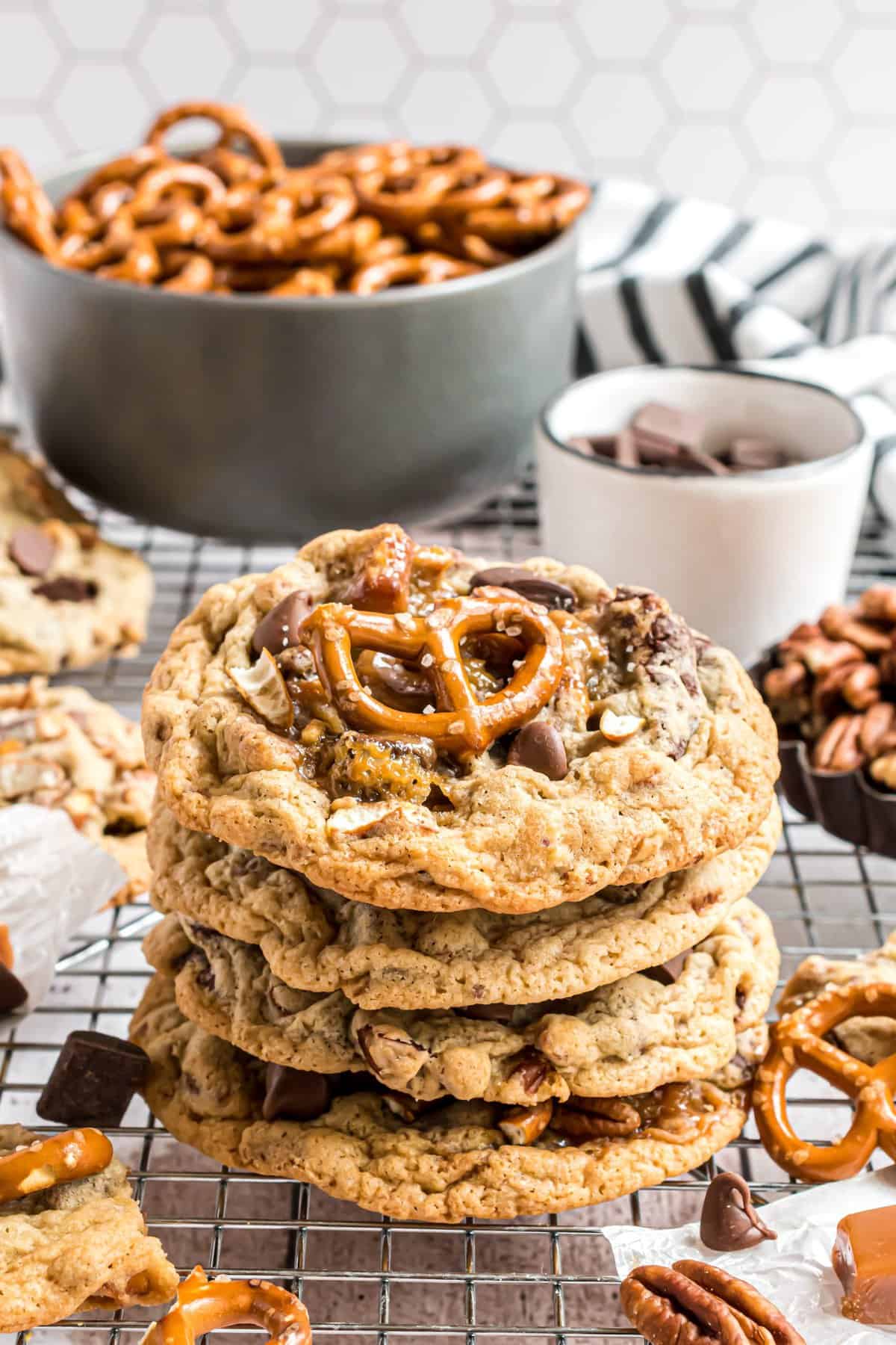 Four stacked cookies on a wire rack with a bowl of pretzels in background. 