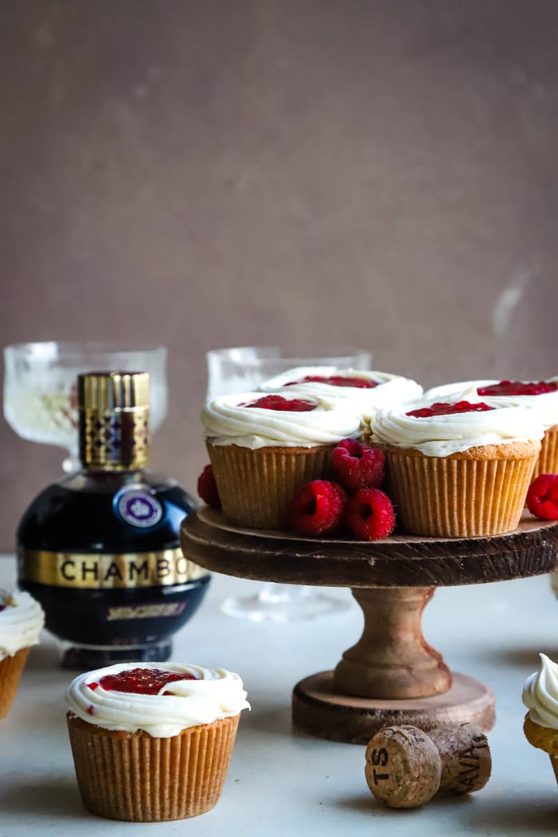 cupcakes on a wood cake stand with bottle of chambered in background. 