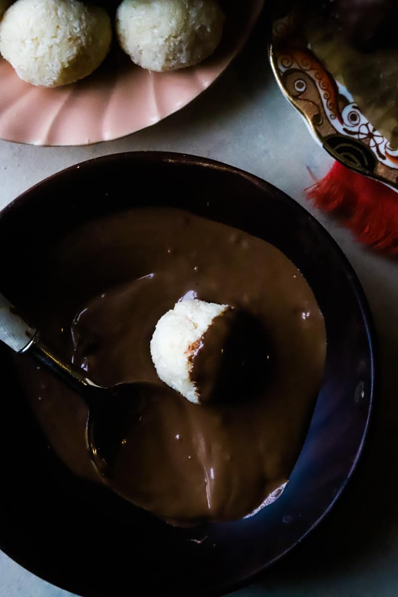 Dipping one balls into a black bowl with melted chocolate. 