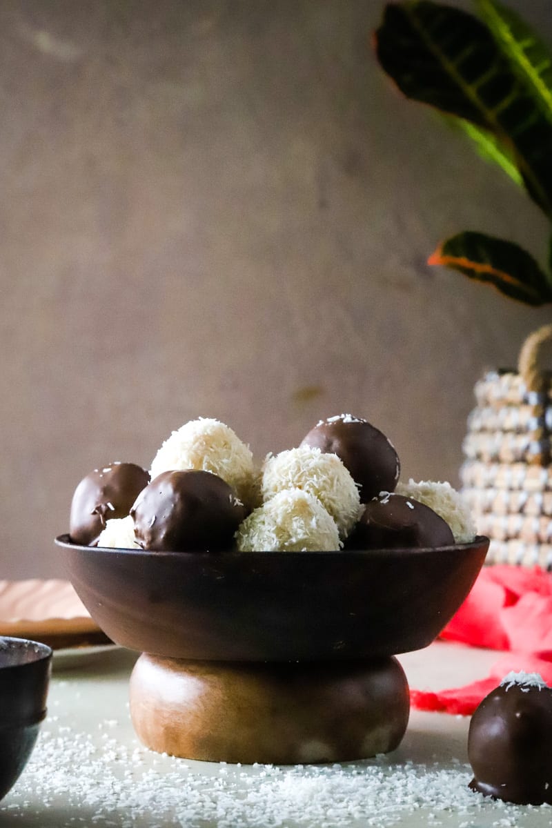 Wooden bowl filled with coconut balls and chocolate dipped balls, beige background. 