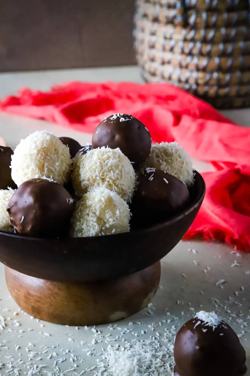 Up close shot of the coconut balls in wooden ball with pink dishtowel next to it. 