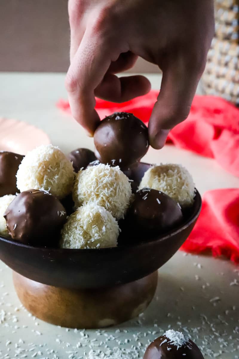 Hand grabbing a chocolate dipped coconut ball from bowl. 