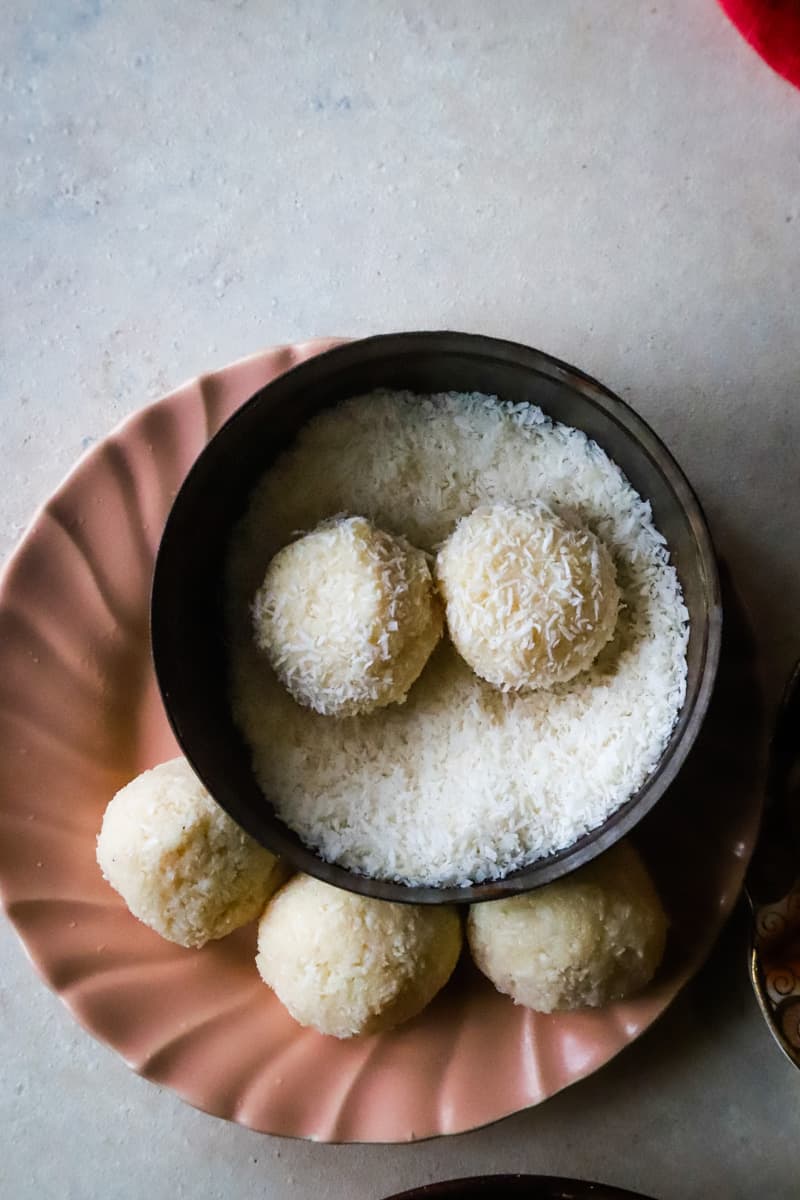 balls on a peach plate with small bowl of extra coconut for rolling the balls into. 