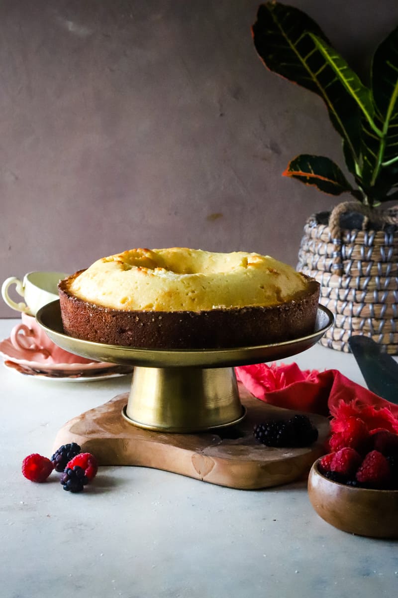 Pound cake on a gold cake stand with plant in the background. 