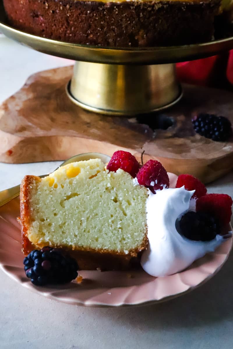 Slice of pound cake with whopped cream and berries on a pink plate. 