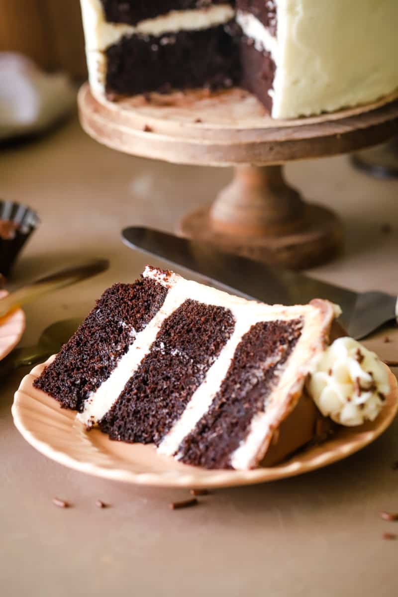 Three layered chocolate cake slice on a peach dish on wood background. 