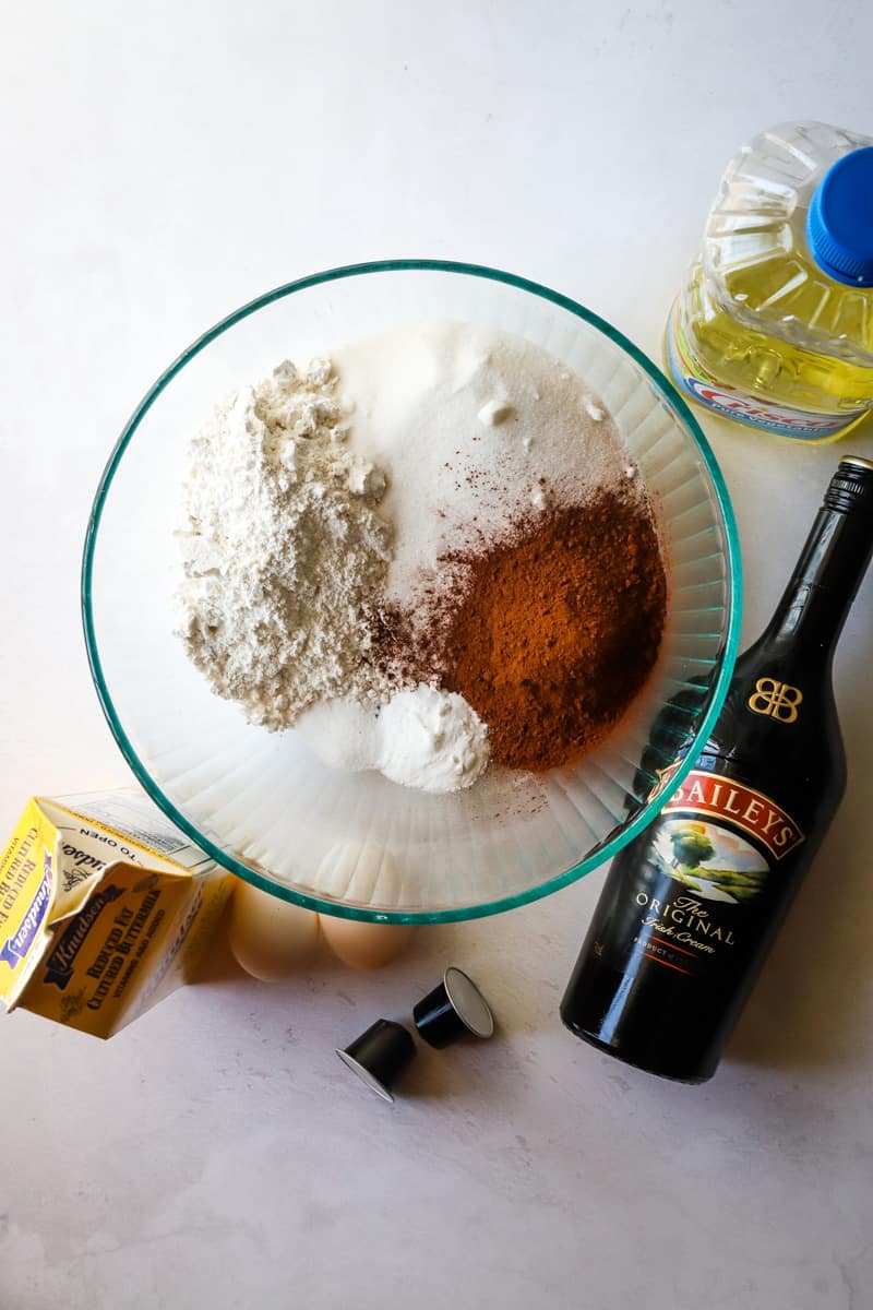 Dry ingredients in a large glass bowl with the bottle of baileys off to the side. 