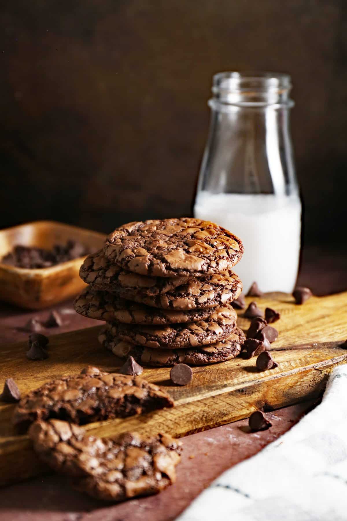 Cookies stacked on a wood cutting board with jar of milk in background. 