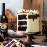 Cake with slices removed on wood cake stand with bottle of baileys in background.