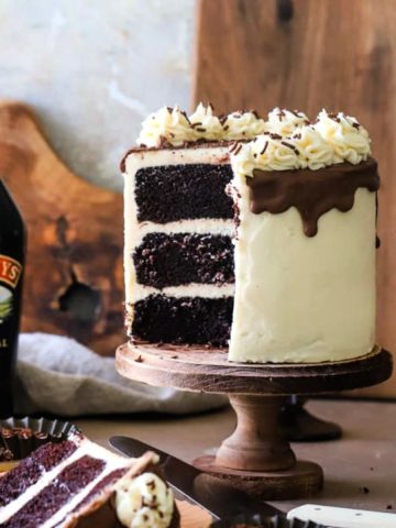 Cake with slices removed on wood cake stand with bottle of baileys in background.