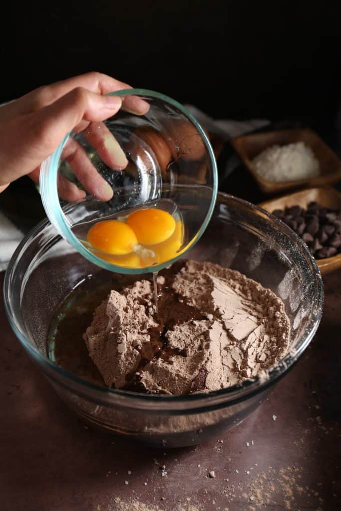 Hand adding the egg yolks to the brownie mix in bowl. 
