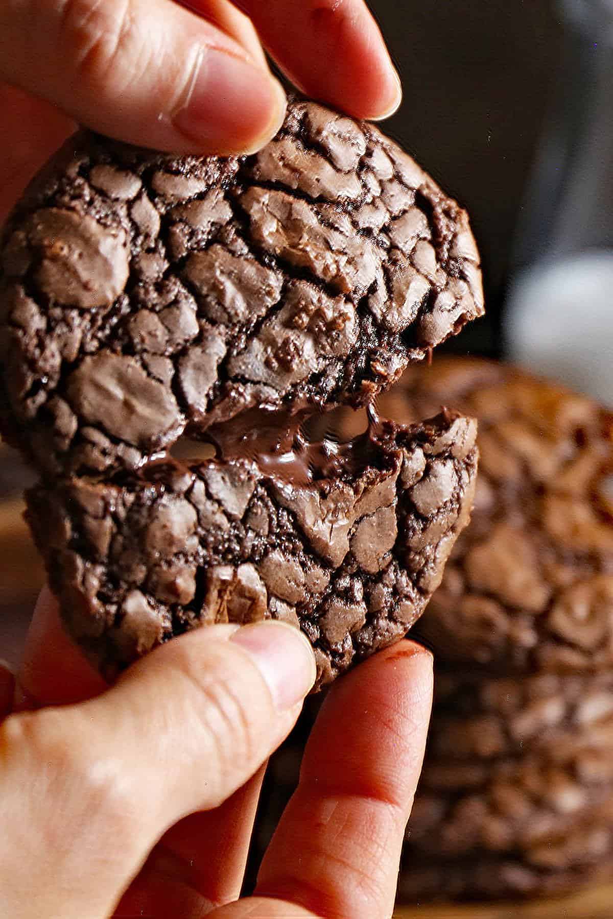 Hand breaking apart the cookie showing the fudgy interior. 