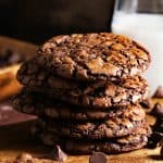 Stacked chocolate crinkle brownie cookies on dark wood background.