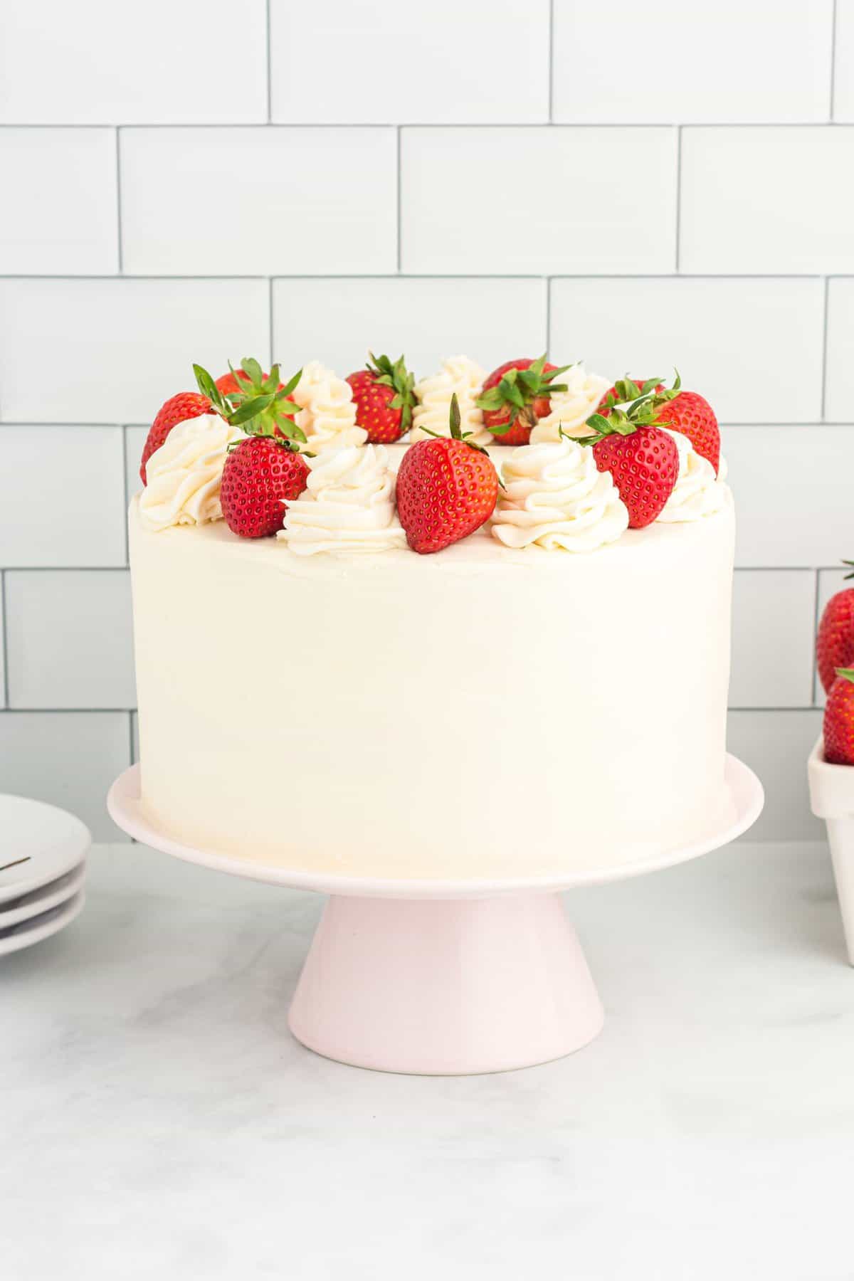 A white cake with fresh strawberries on the top on a pink cake plate. 