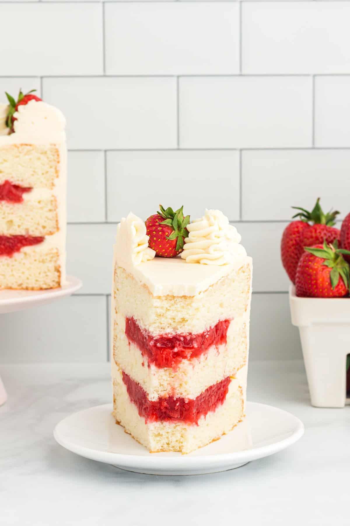 Slice of cake on a white plate with a bowl of strawberries in the corner. 