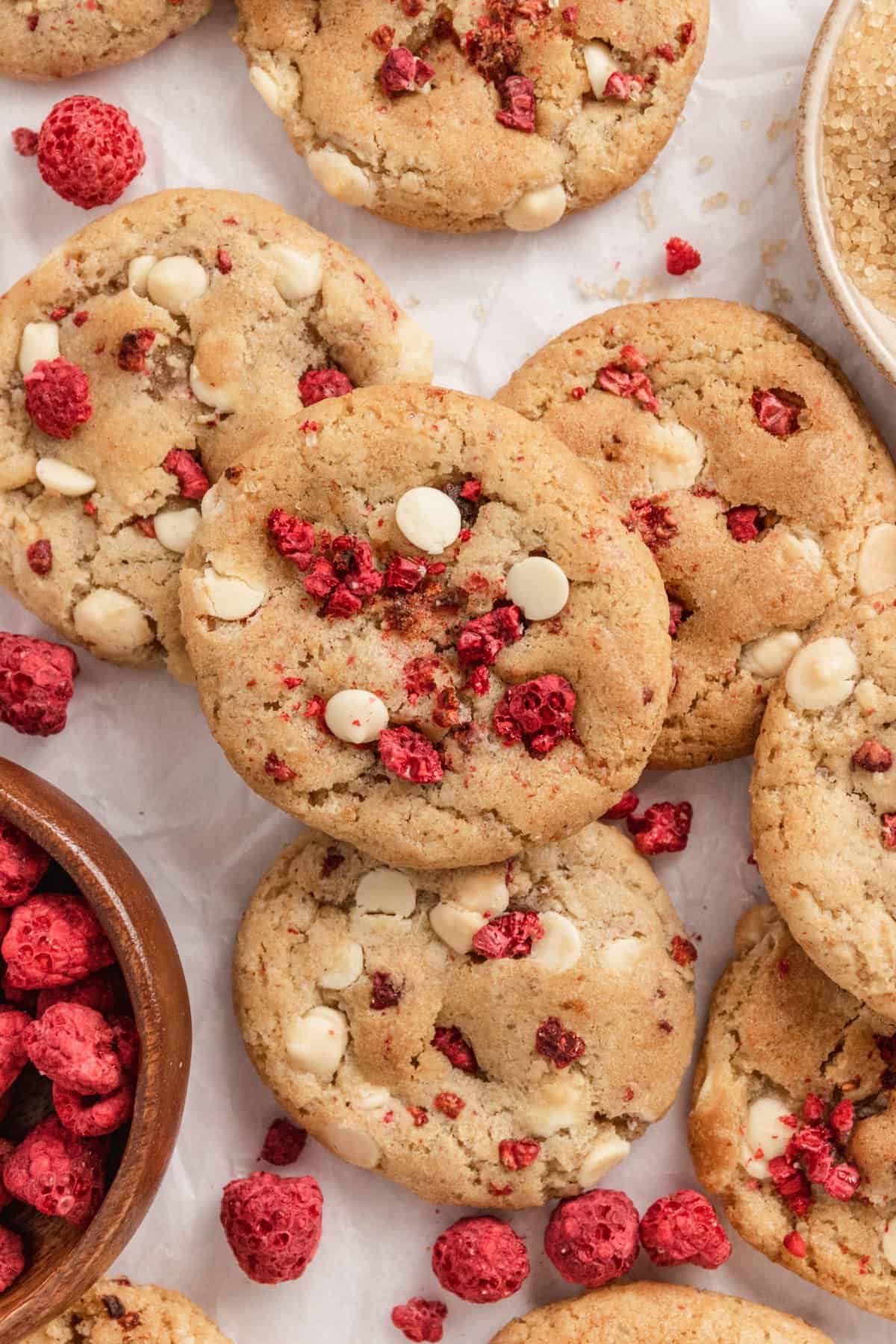 Overhead shot of cookies laid out on a white parchment background with raspberries. 