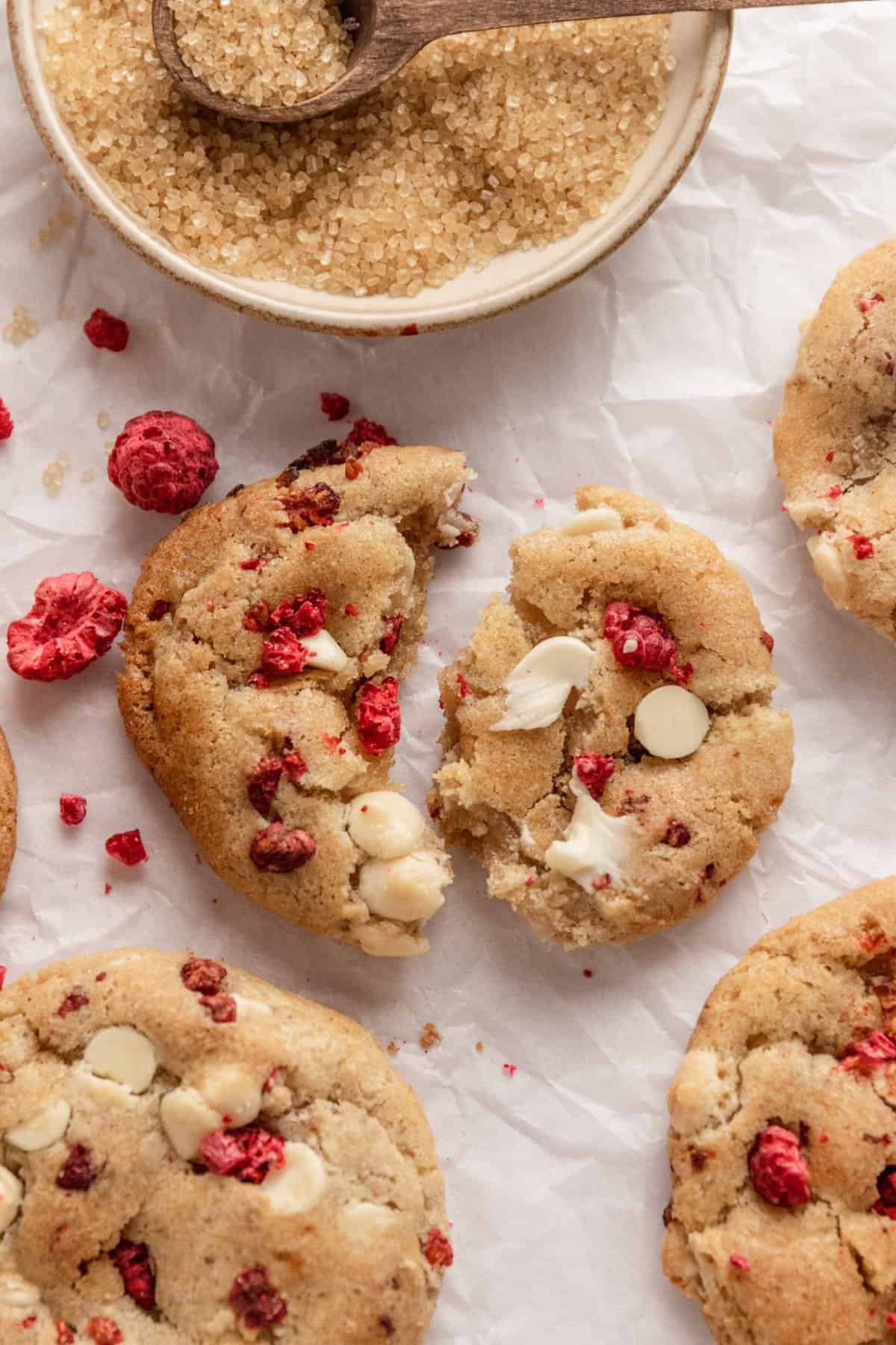 Cookies on a piece of white parchment with middle cookie broken in half and dried raspberries around it. 
