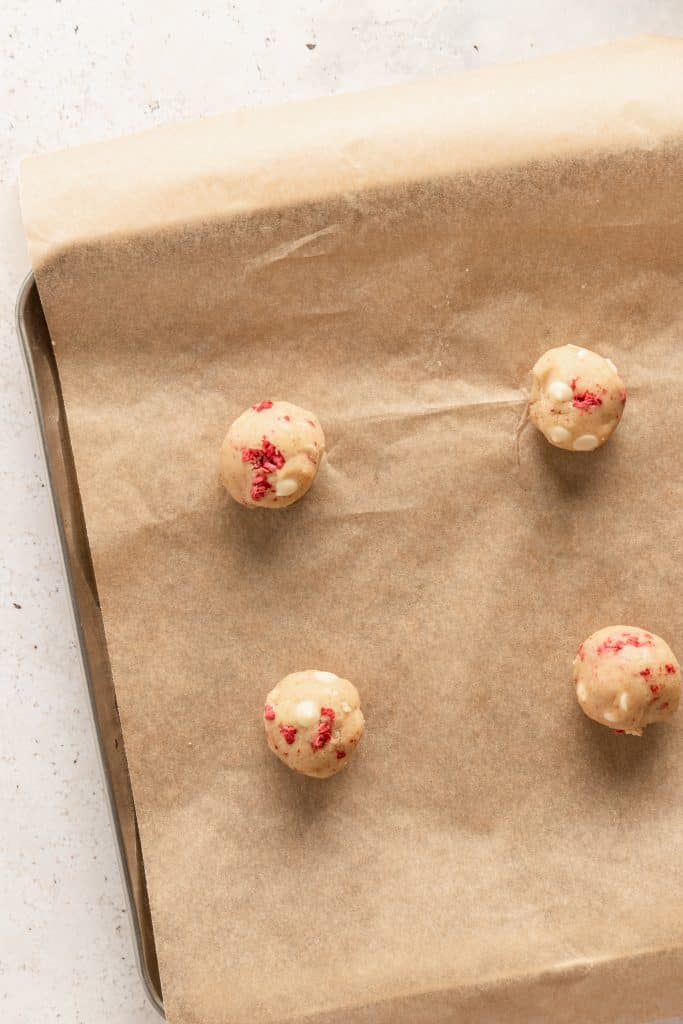 Scooped and rolled cookie dough balls on a brown parchment lined cookie sheet. 
