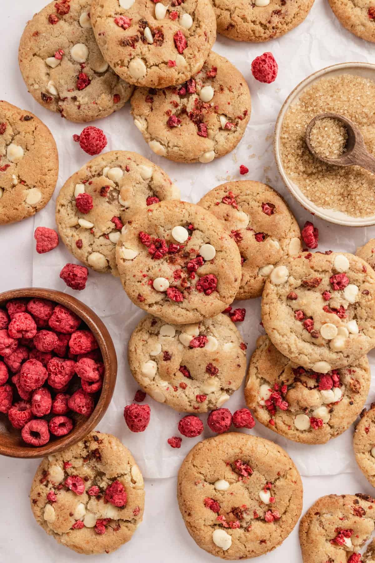 Cookies spread out on a white background with bowl of dried raspberries. 