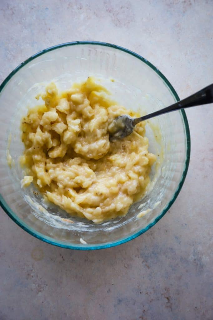 Mashed banana and fork in a large glass bowl. 