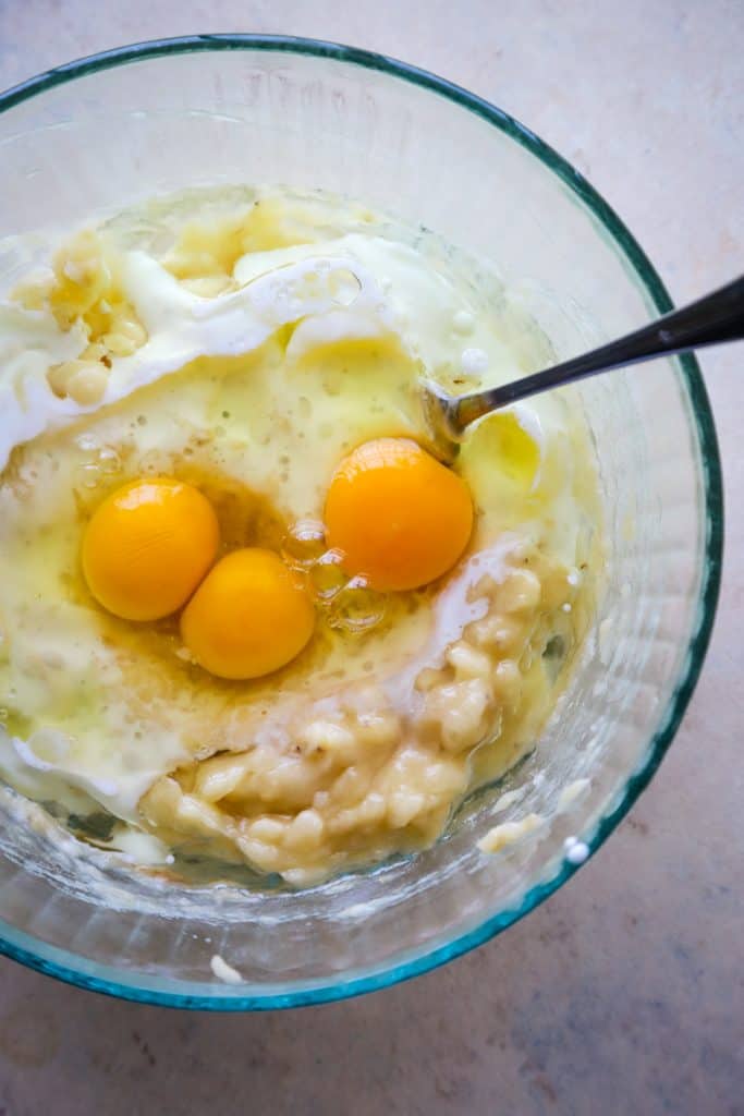 Adding eggs and milk to the bowl of mashed bananas. 