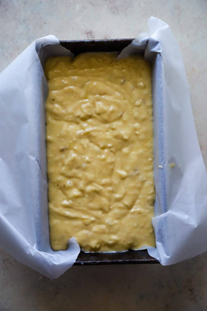 Banana bread batter poured into a loaf pan lined with parchment paper. 