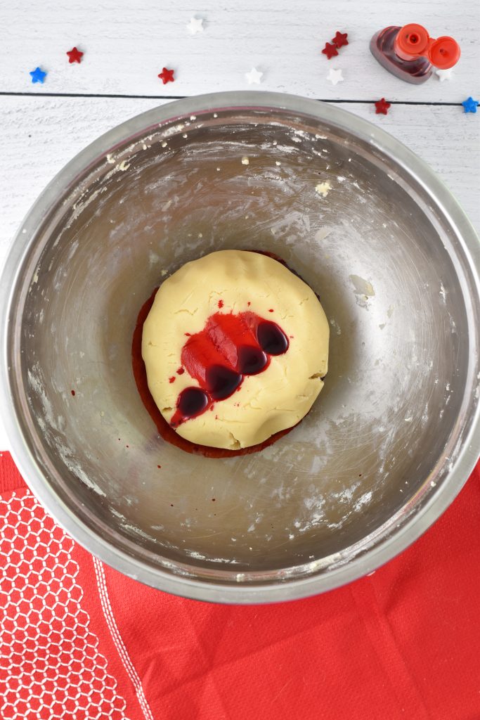 Adding red food dye to a ball of sugar cookie dough in metal bowl. 