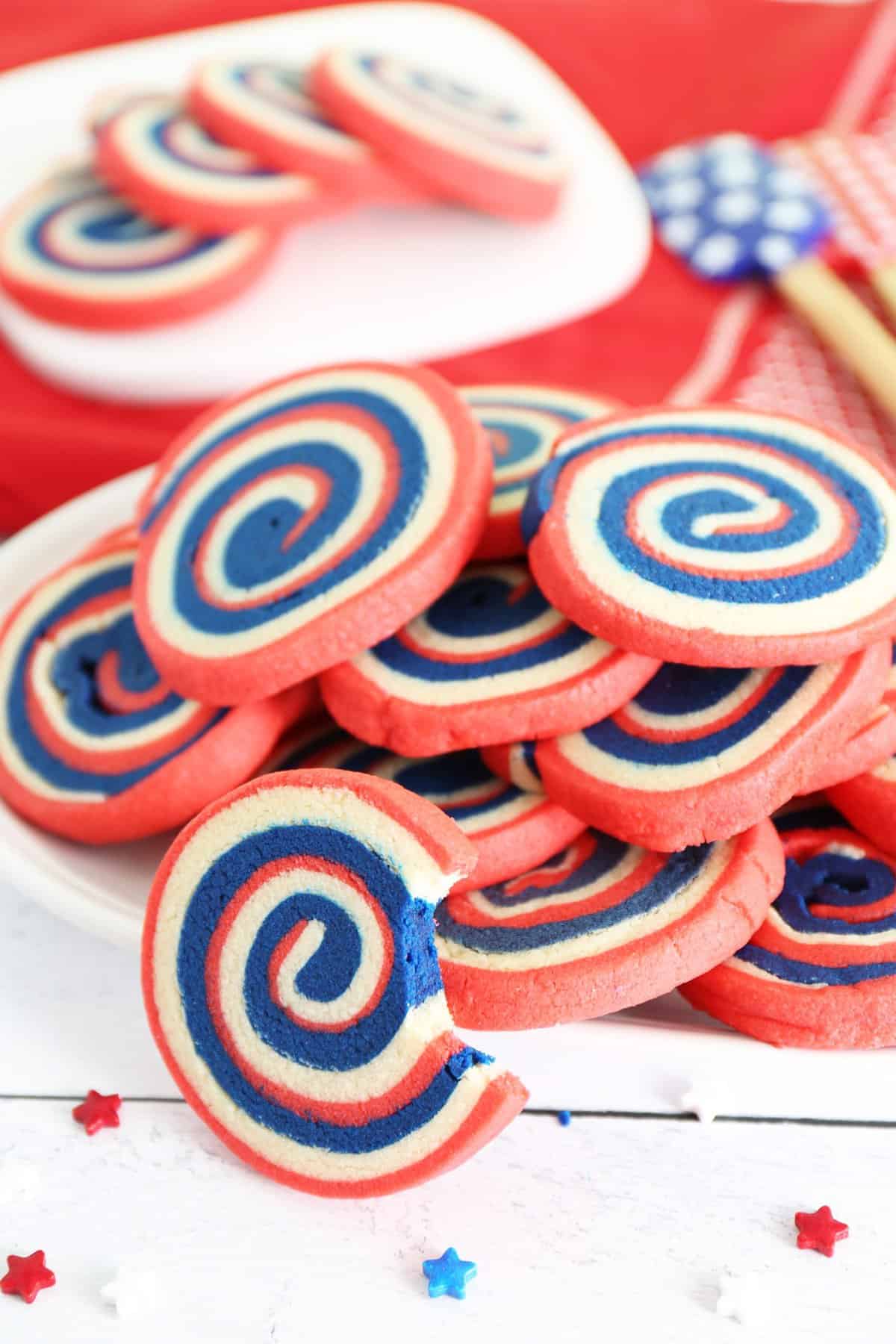 White plate stacked with red white and blue pinwheel cookies with red background. 