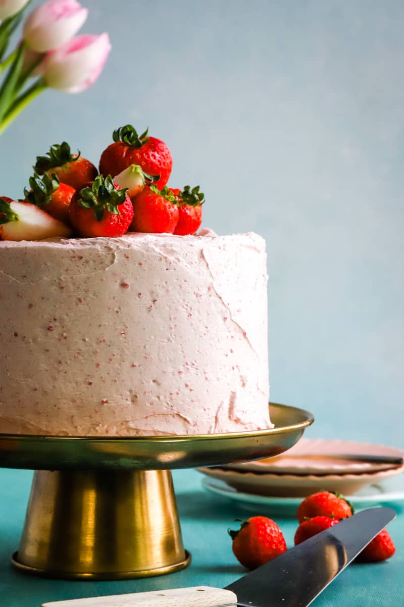Strawberry cake topped with fresh strawberries on a gold cake plate. 
