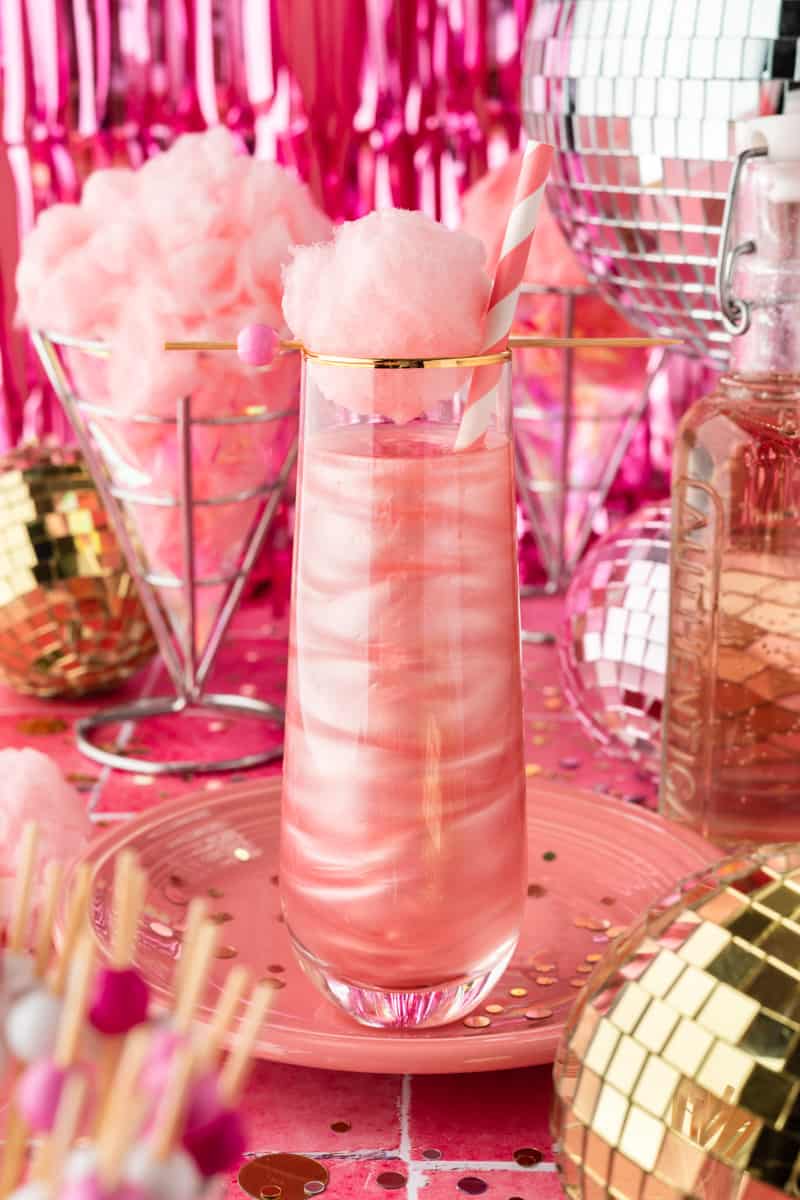 Pink shimmery cocktail in tall stemless champagne flute and pink background. 