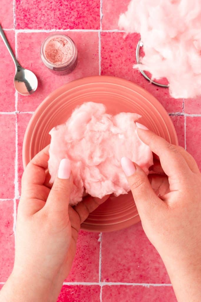 hands flattening out cotton candy on a pink plate and pink background. 