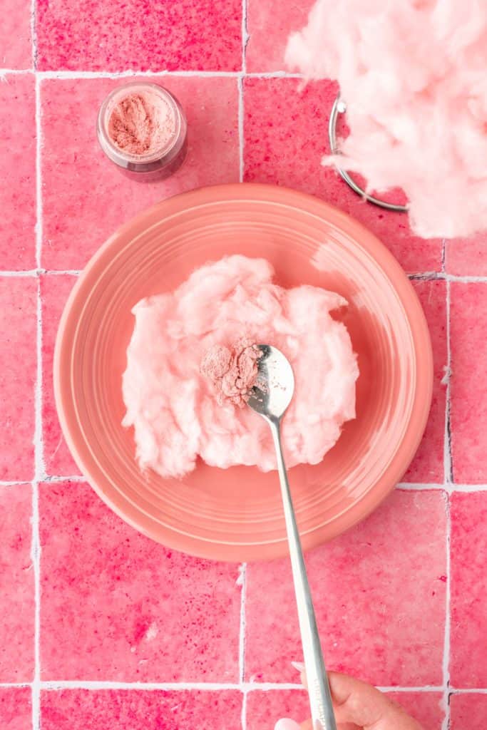 Spoon adding the edible luster dust to the flattened pink cotton candy. 
