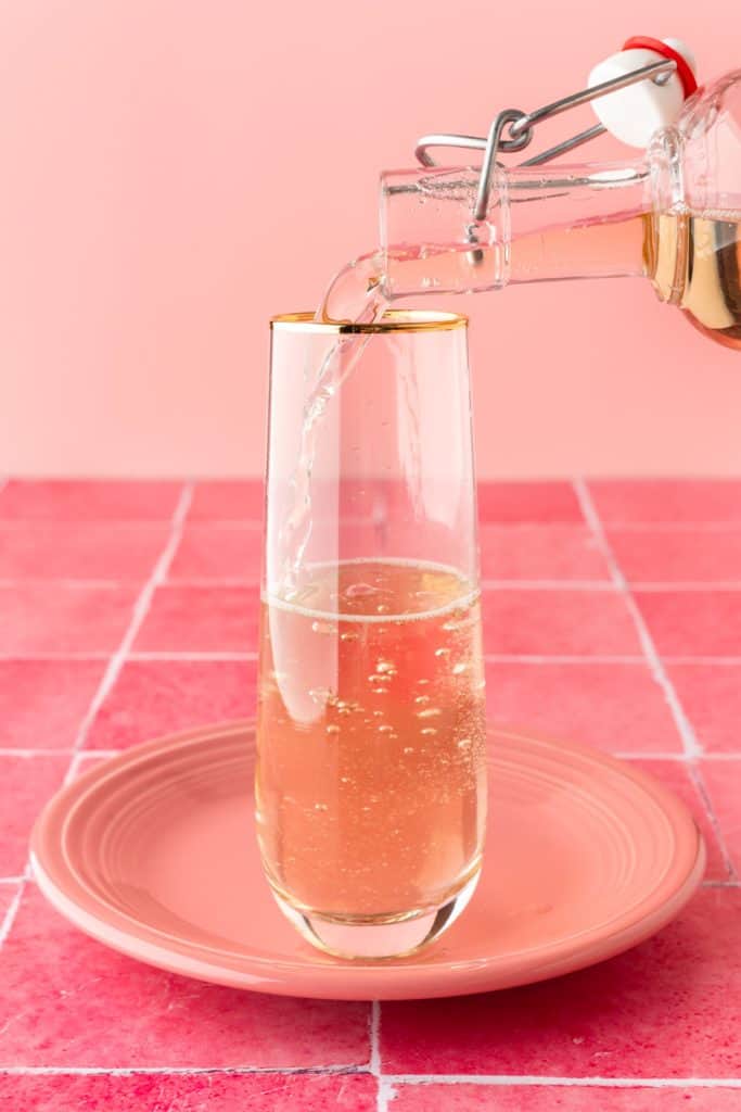 Hand adding a bottle of ginger ale to glass on pink background. 