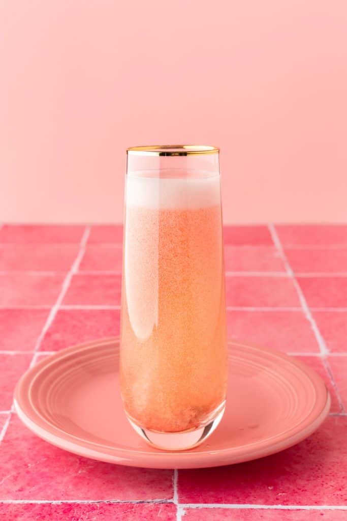 Cocktail in glass on pink plate with pink tile background. 
