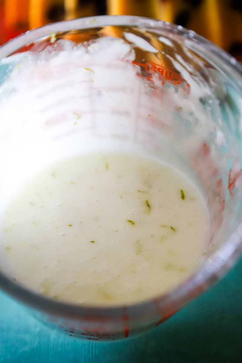 The lime coconut glaze in a measuring cup with specs of lime zest. 