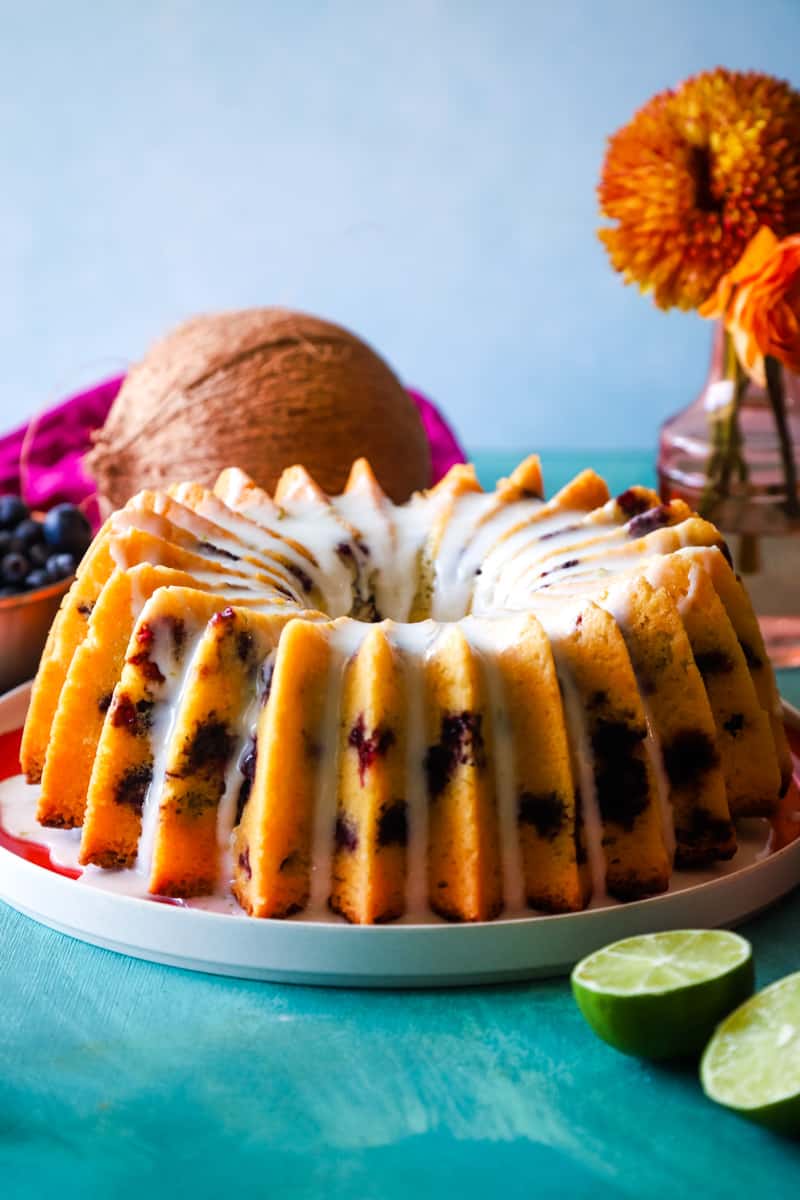 Bluberry coconut lime bundt cake with lime glaze on a red plate with lime wedges around it. 